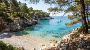 Piccola cala tranquilla con acqua cristallina, pini e barche a vela ancorate in lontananza