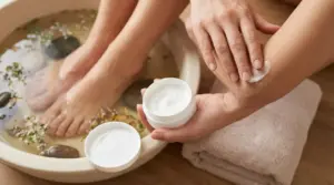 Una persona mentre applica una crema sul gomito accanto a un pediluvio con erbe