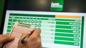 Persona compila una schedina del SuperEnalotto davanti a uno schermo con premi e combinazioni
